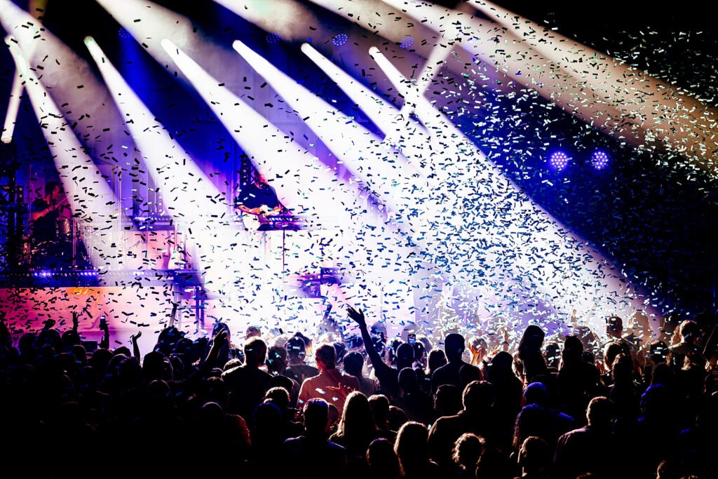 Konzert mit Publikum und Konfetti unter Lichtstrahlen.