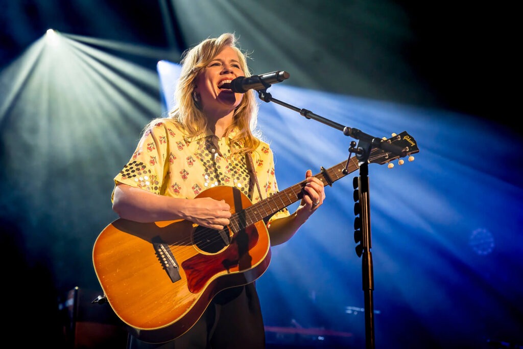 Frau singt und spielt Gitarre auf der Bühne.