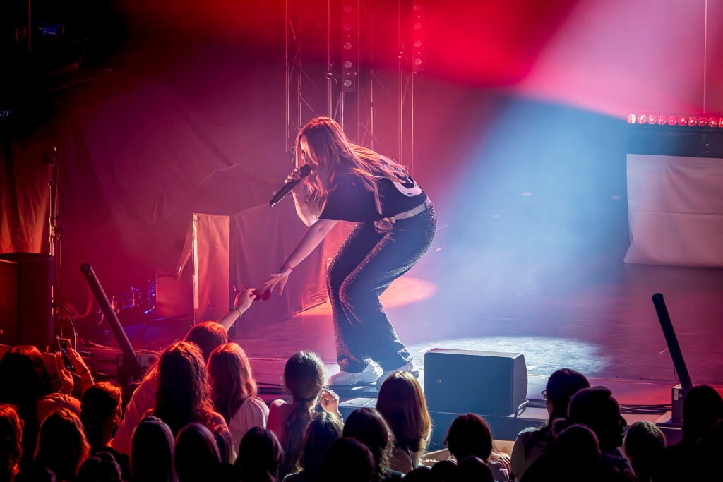 Sängerin auf Bühne mit Mikrofon, rotes Licht.