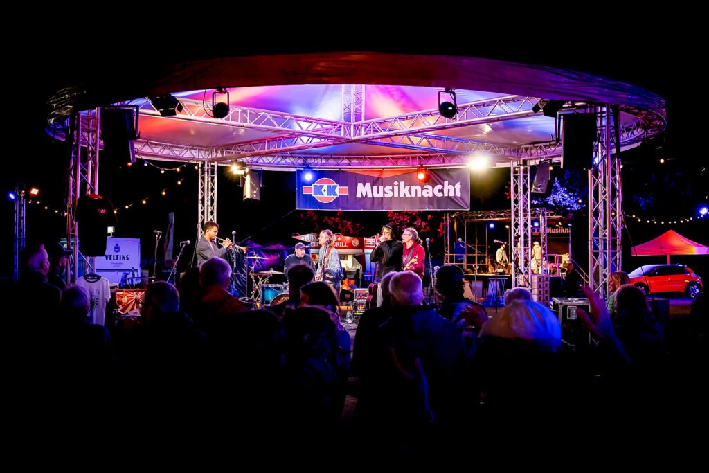 Band spielt auf beleuchteter Bühne während Musikevent.