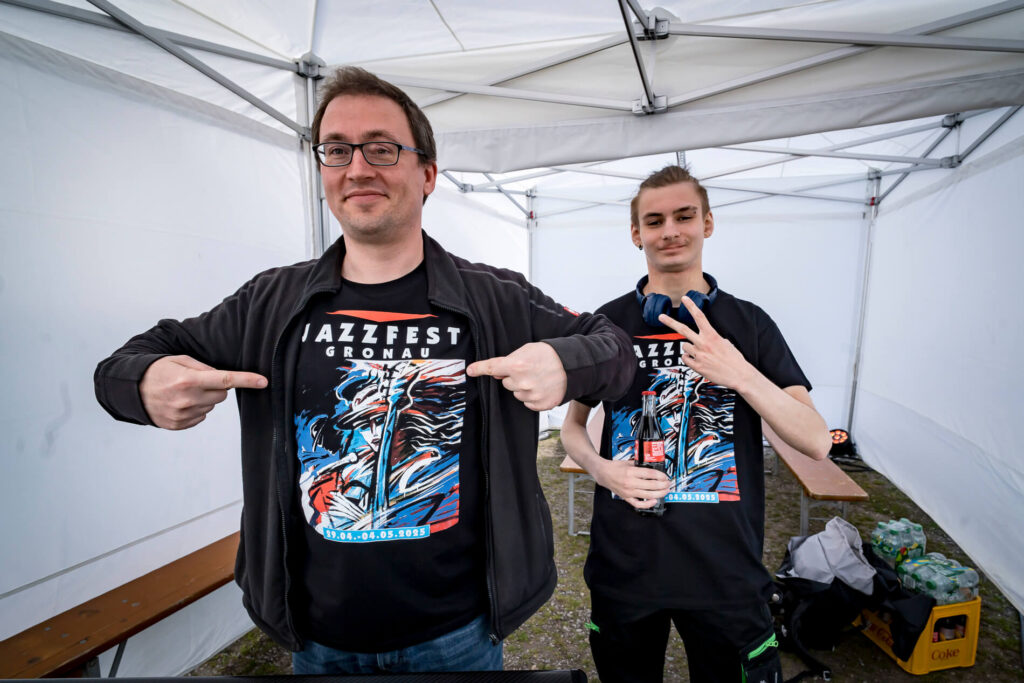 Zwei Männer tragen Jazzfest Gronau T-Shirts im Zelt.