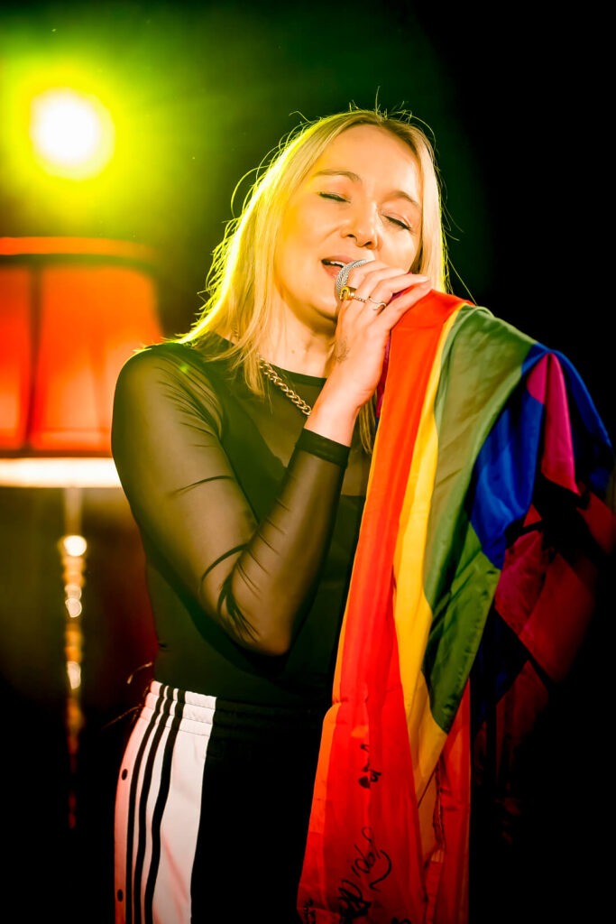 Frau singt mit Regenbogenflagge auf Bühne.
