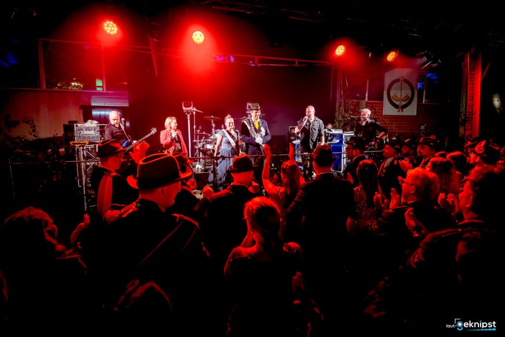 Band spielt auf roter beleuchteter Bühne vor Publikum.