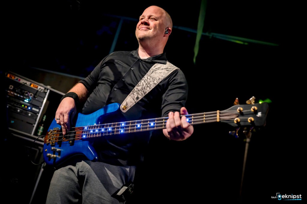 Bassist spielt blaue E-Gitarre auf Bühne.