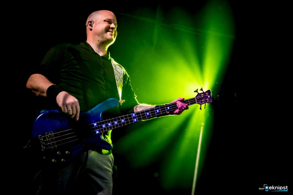 Musiker spielt E-Bass auf Bühne im grünen Licht.