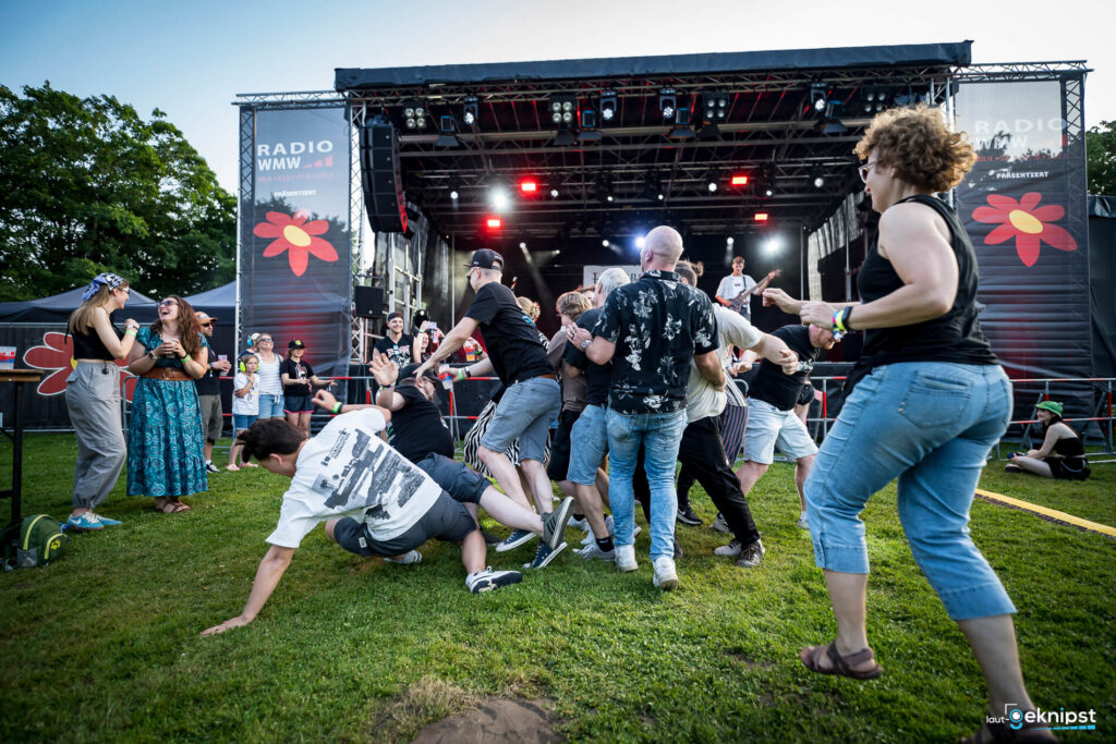 Menschen tanzen wild bei Outdoor-Konzert vor Bühne.