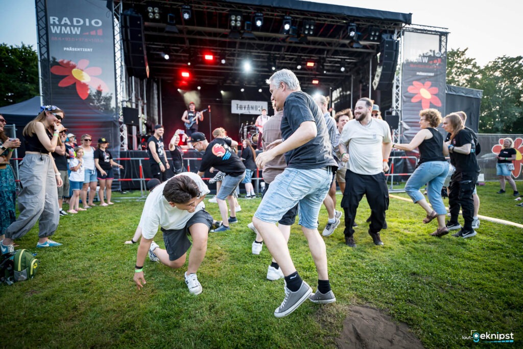Menschen tanzen vor einer Konzertbühne im Freien.