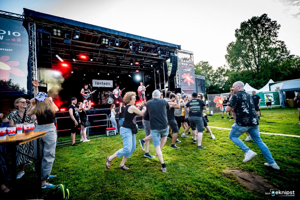 Live-Band spielt auf Festivalbühne, Publikum tanzt im Freien.