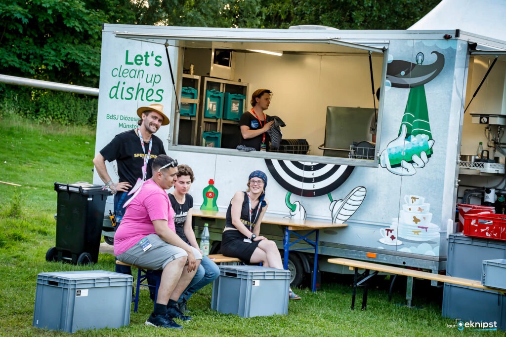 Gruppe entspannter Menschen vor Spülstation auf Festival.