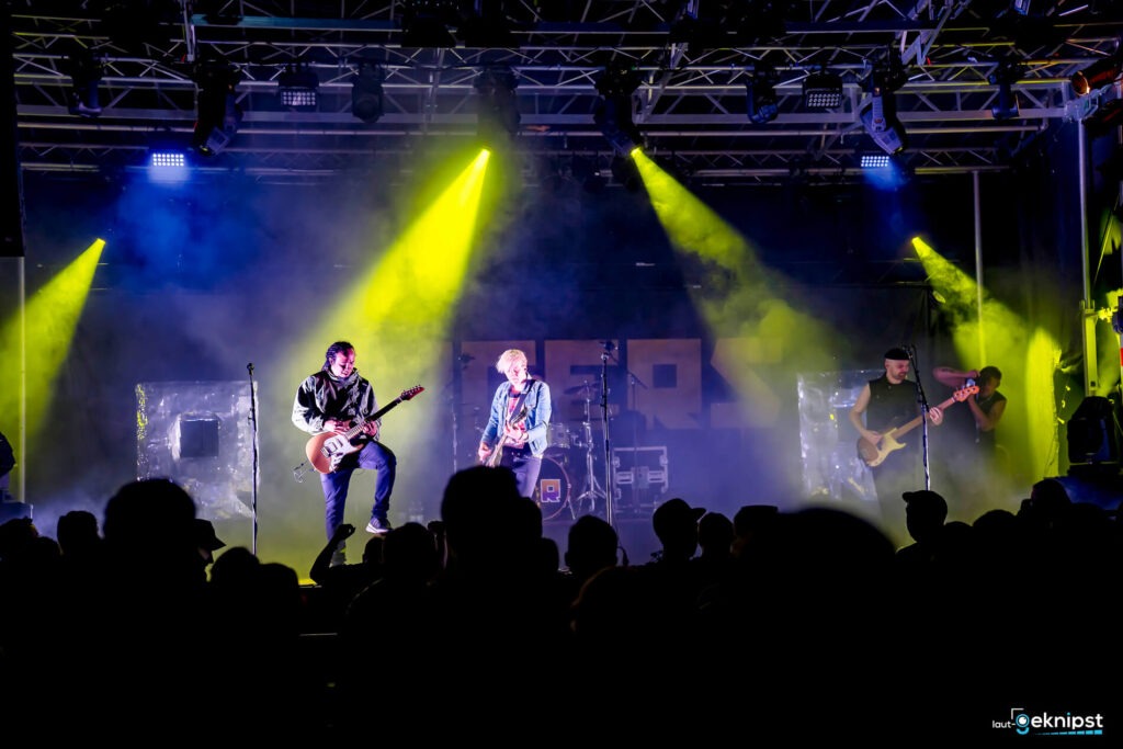 Band spielt auf beleuchteter Bühne vor Publikum.
