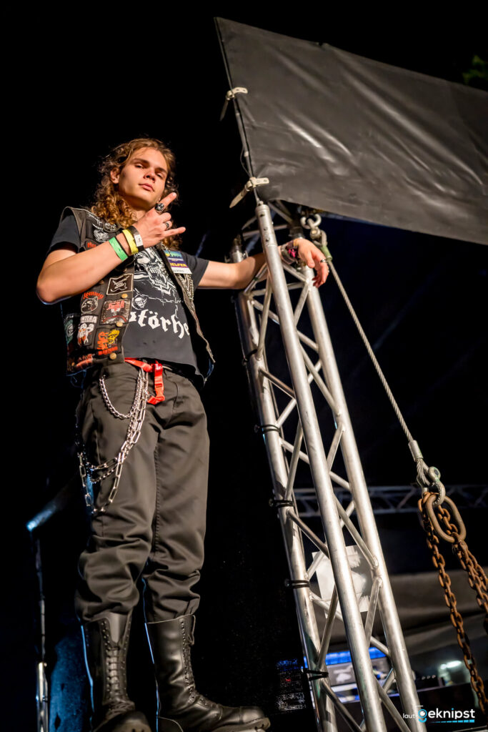 Rocker posiert auf Bühne mit Metal-Zeichen.
