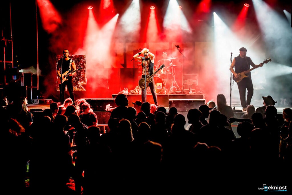 Rockband spielt auf beleuchteter Bühne vor Publikum.