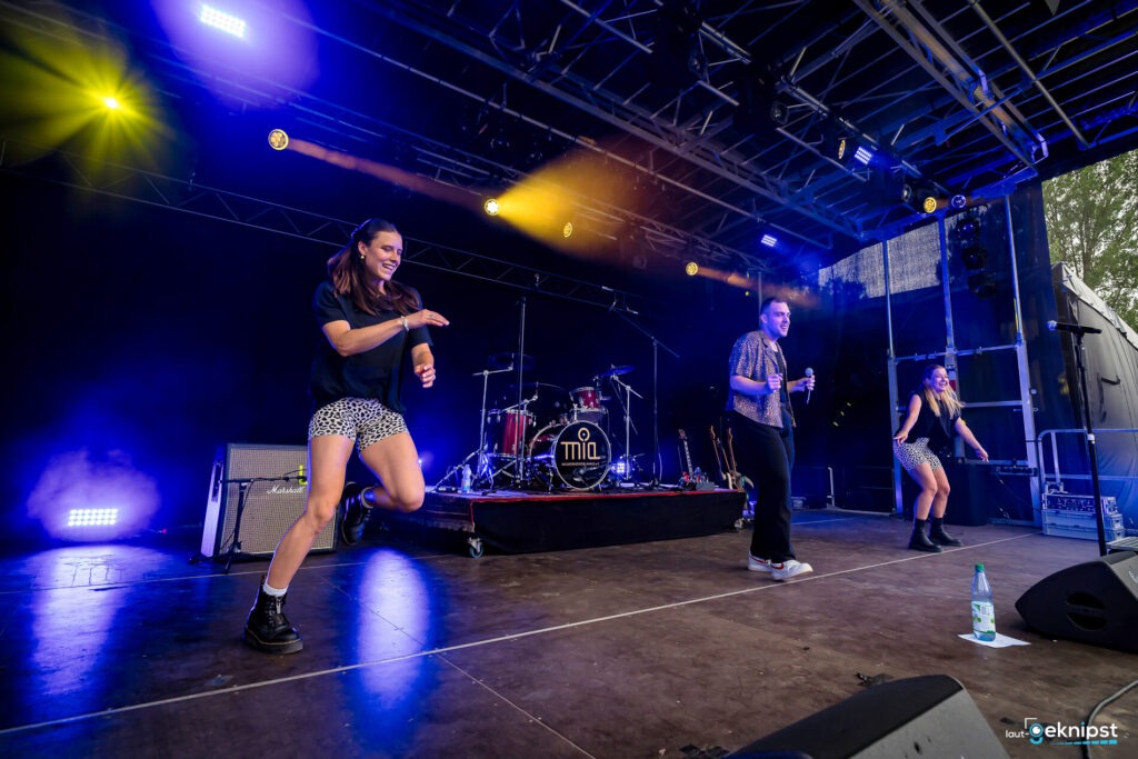 Drei Personen performen auf einer Bühne mit buntem Licht.