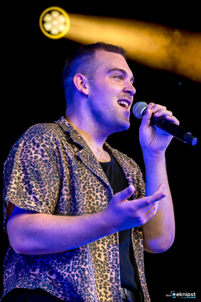 Mann singt auf der Bühne mit Mikrofon.