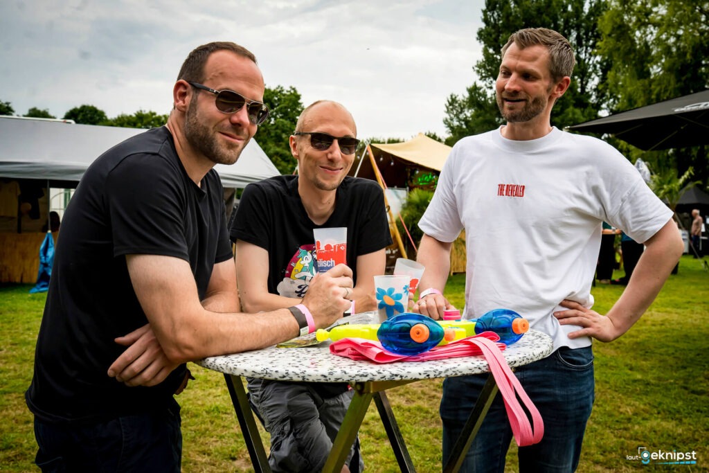 Drei Männer stehen am Tisch im Freien.