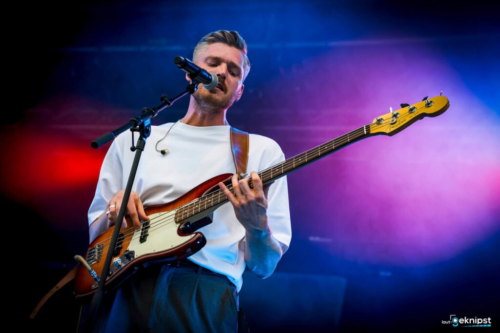 Musiker spielt E-Bass auf Bühne unter buntem Licht.