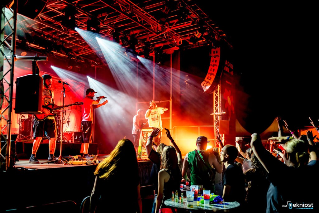 Band spielt auf einer Bühne mit Publikum, bunte Lichter.
