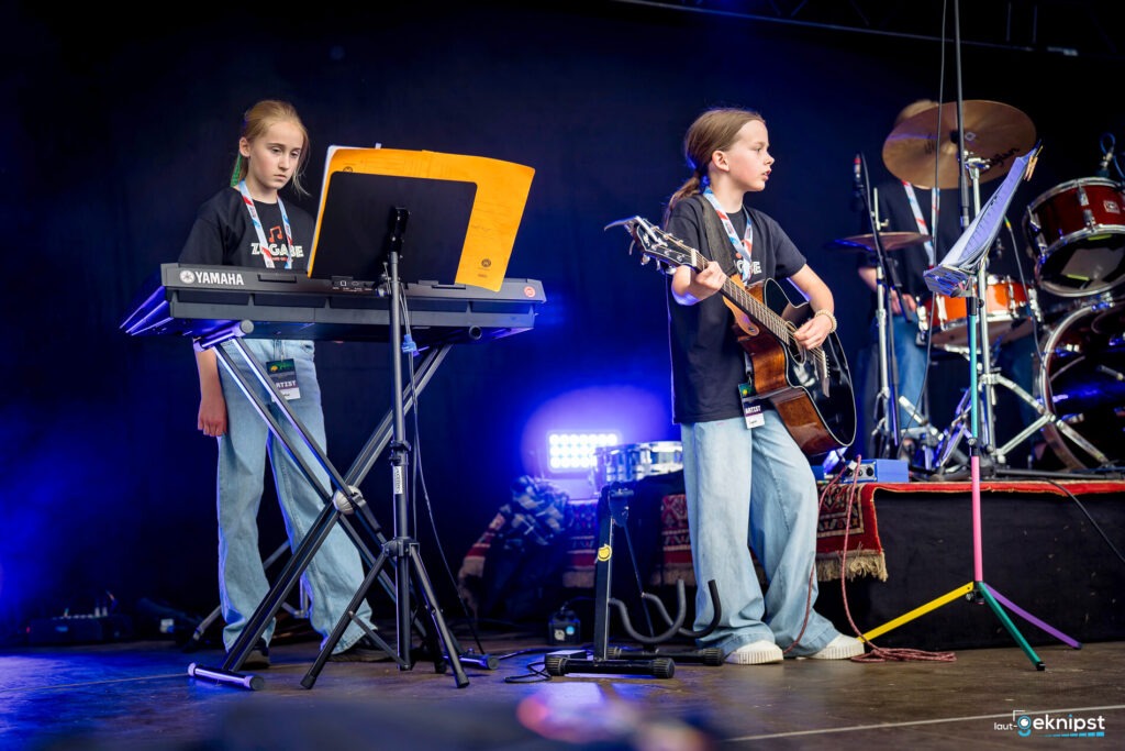 Kinderband spielt Keyboard und Gitarre auf der Bühne.