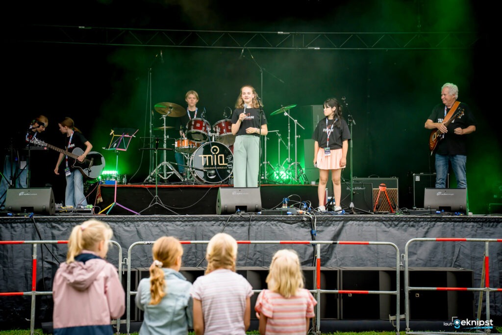 Kinderband auf Bühne, grünes Licht, Publikum im Vordergrund.