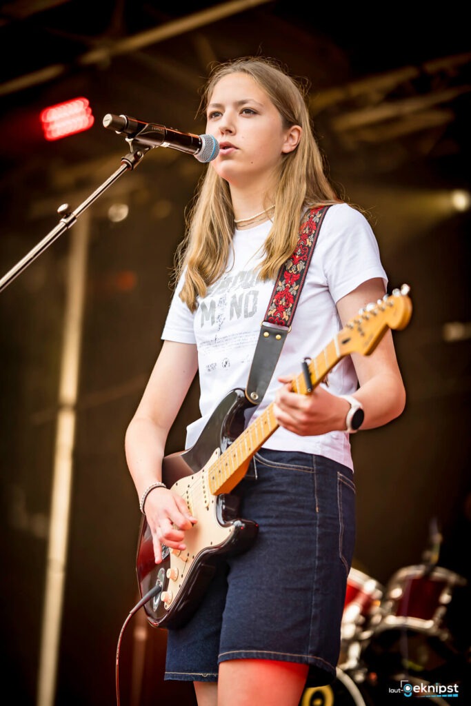 Musikerin spielt E-Gitarre auf Bühne.