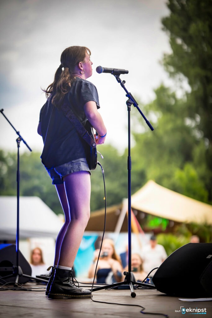 Gitarristin singt auf Festivalbühne, Zuschauer applaudieren.