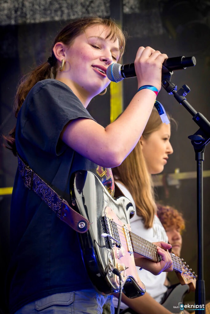 Junger Musiker singt und spielt Gitarre auf der Bühne.