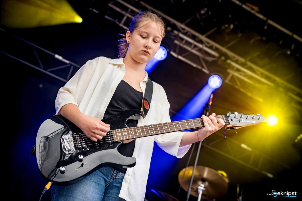 Junge Frau spielt E-Gitarre auf der Bühne.