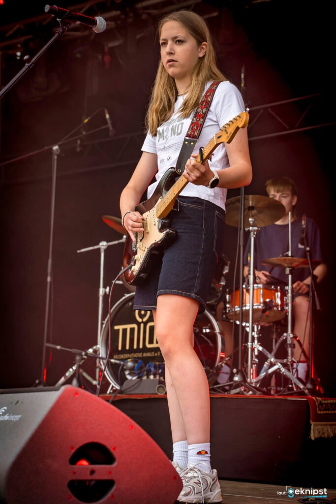 Junge Musikerin spielt Gitarre auf der Bühne.