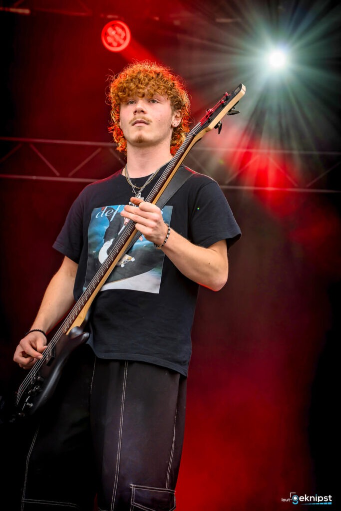 Mann spielt Bass auf Bühne mit rotem Licht.