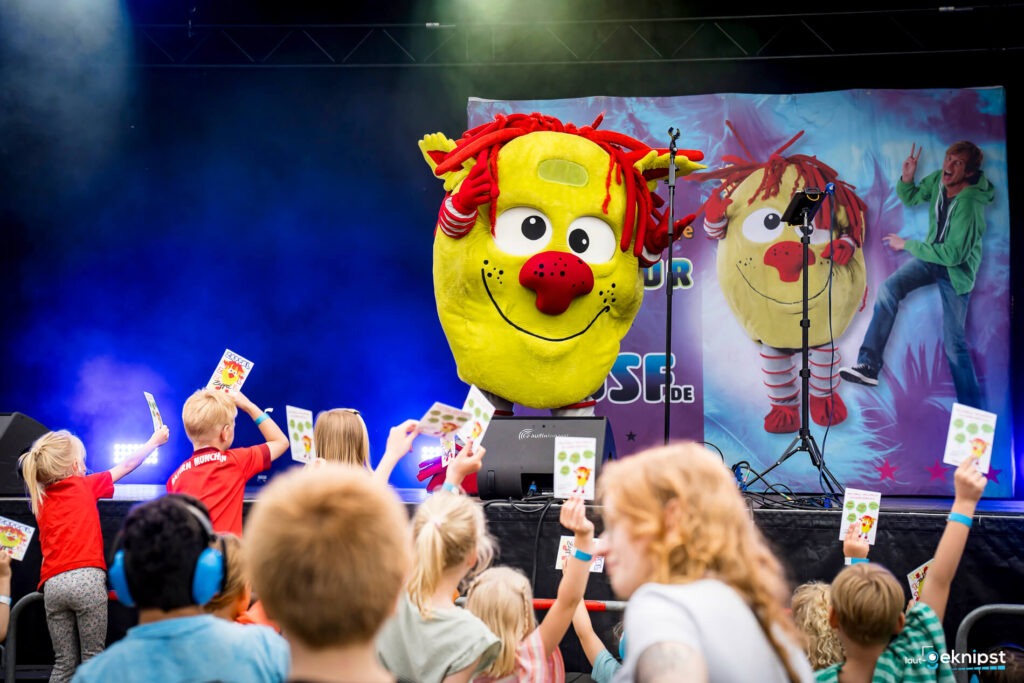 Kinder freuen sich über großes Maskottchen auf der Bühne.