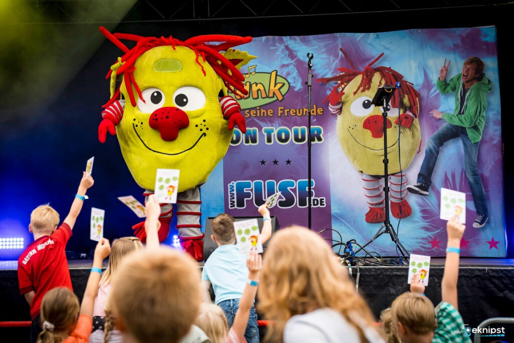 Bunte Figur auf einer Kinderbühne, Publikum mit Karten.