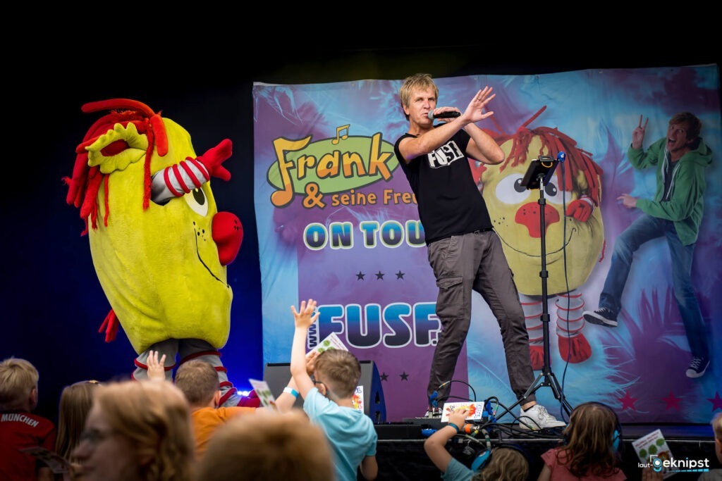 Kinderkonzert auf der Bühne mit buntem Maskottchen.