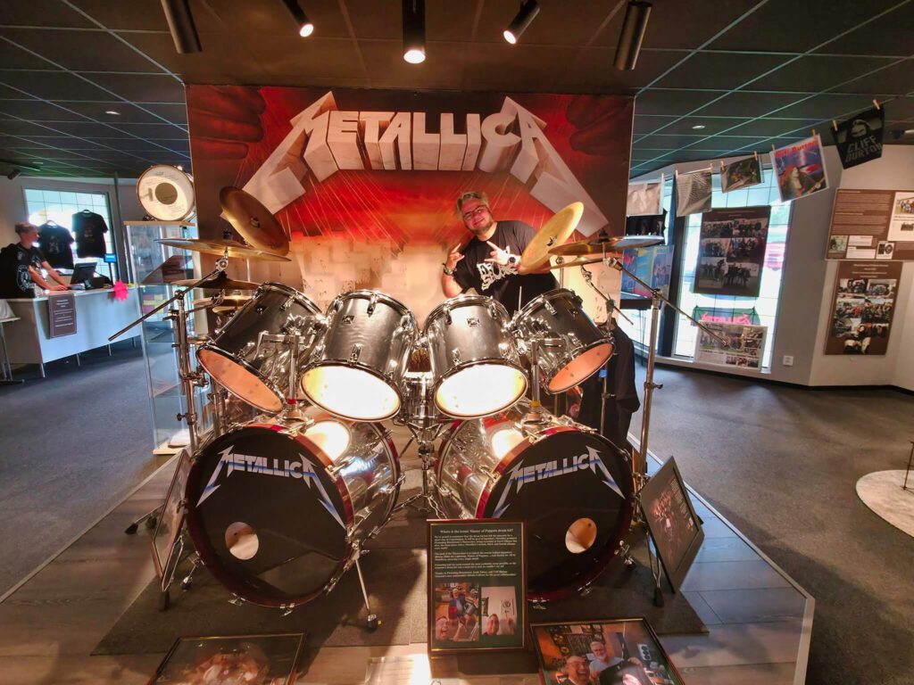 Person spielt Schlagzeug im Metallica-Raum.