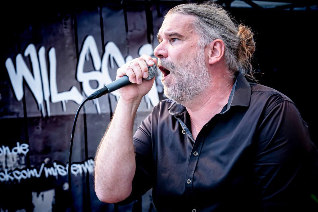 Mann singt leidenschaftlich ins Mikrofon auf Bühne.