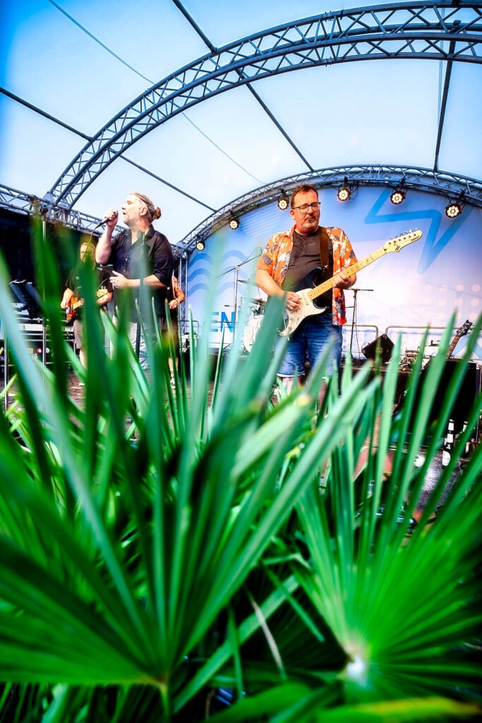Band spielt live auf Open-Air-Bühne hinter Pflanzen