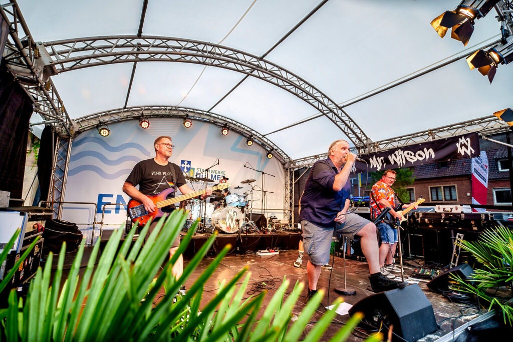 Band spielt Live-Konzert auf überdachter Bühne.