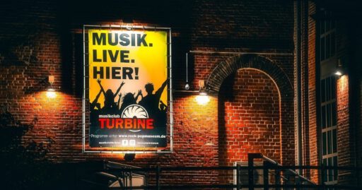 Plakat mit Musik-Event-Werbung an Backsteinwand.