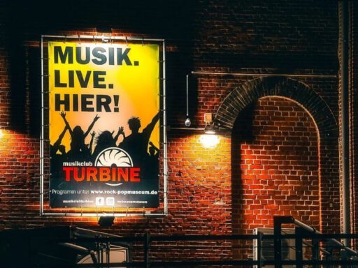 Plakat mit Musik-Event-Werbung an Backsteinwand.