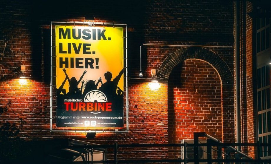 Plakat mit Musik-Event-Werbung an Backsteinwand.