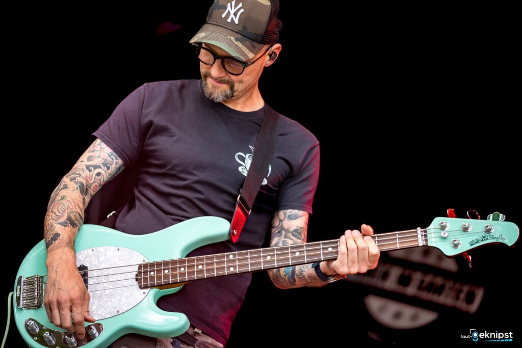 Tätowierter Musiker spielt E-Bass auf der Bühne.