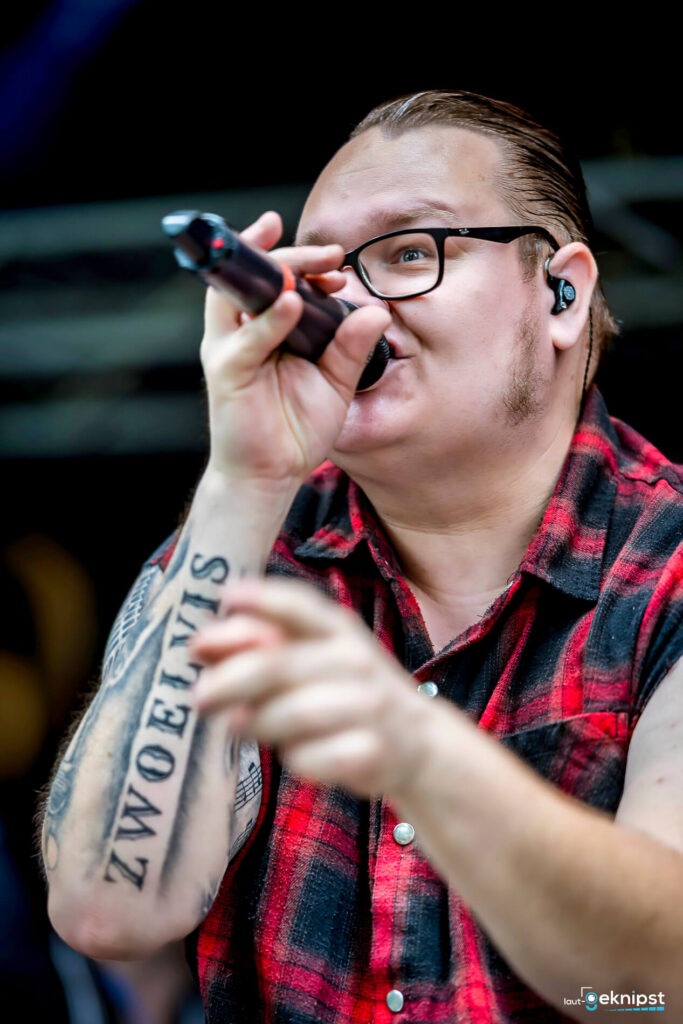 Mann singt in Mikrofon mit Tattootext.