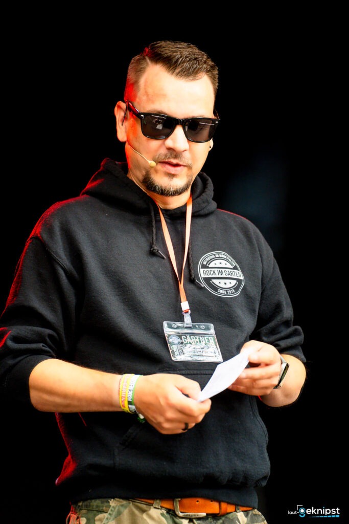 Mann mit Sonnenbrille spricht auf einer Bühne.