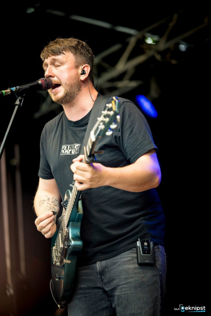 Musiker singt und spielt Gitarre auf der Bühne.