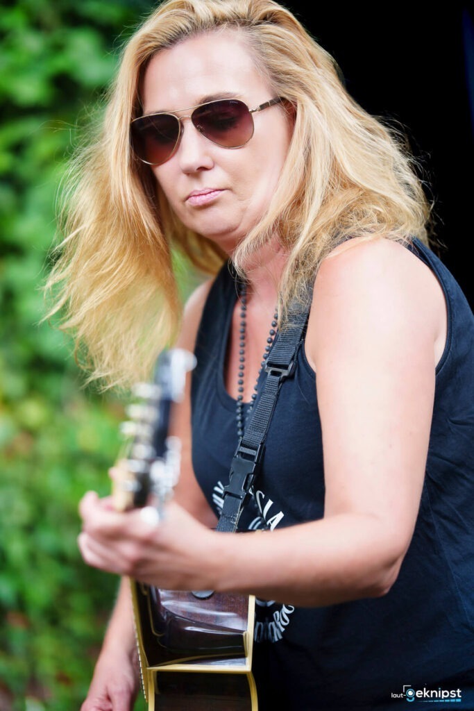 Frau mit Sonnenbrille spielt Gitarre im Freien.