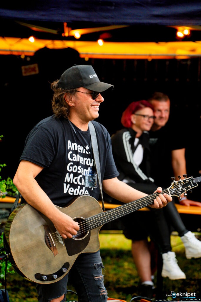 Gitarrenspieler auf der Bühne lächelt im Freien.