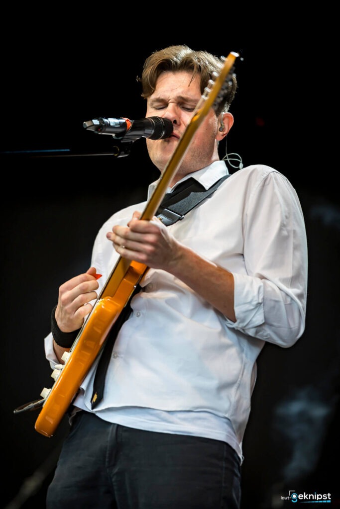 Musiker spielt Gitarre und singt auf Bühne.