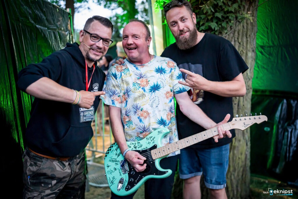 Drei Männer mit Gitarre auf Festival abgebildet.