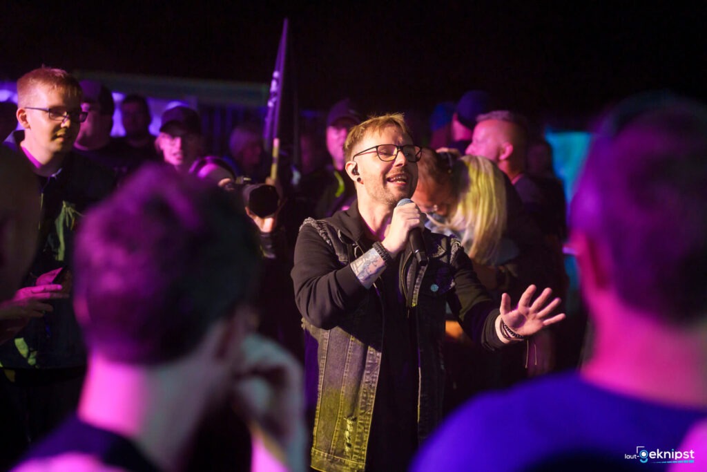 Sänger mit Mikrofon bei Konzert, Publikum im Hintergrund.