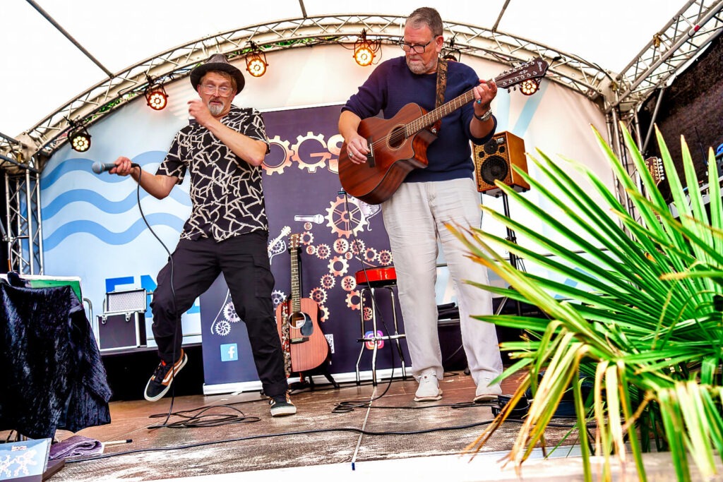 Zwei Musiker auf Bühne mit Gitarre und Mikrofon.
