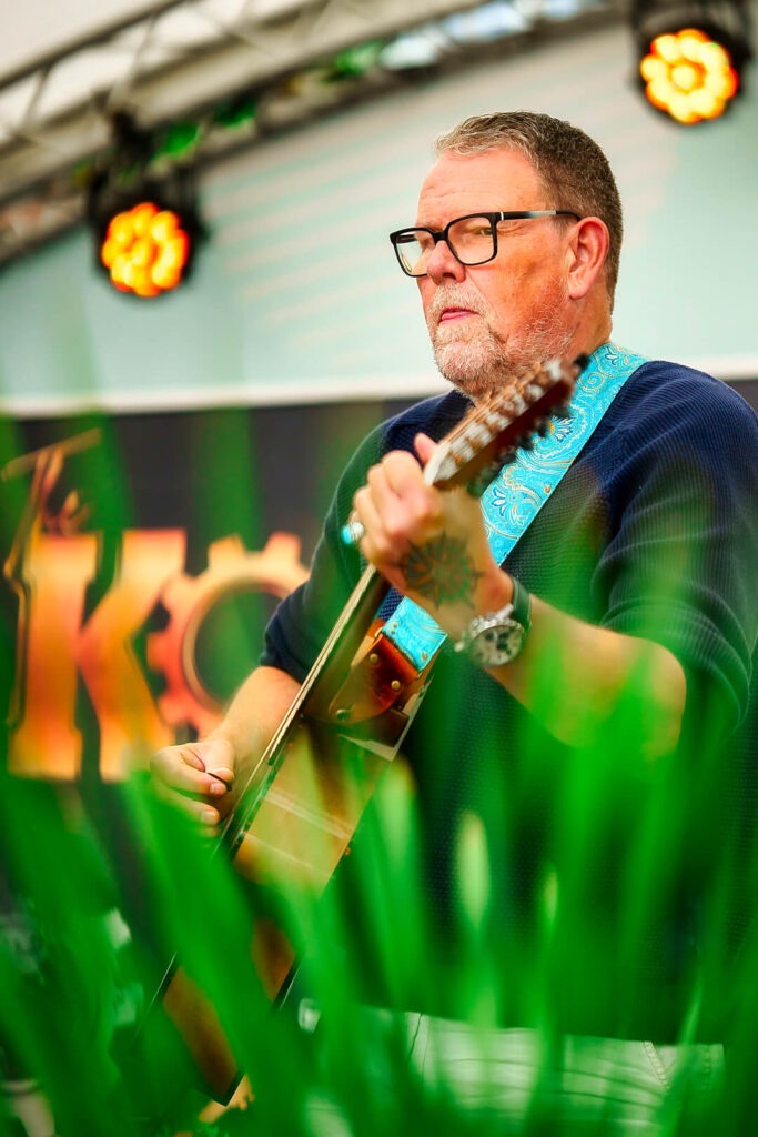Mann spielt Gitarre auf Bühne mit Lichtern.